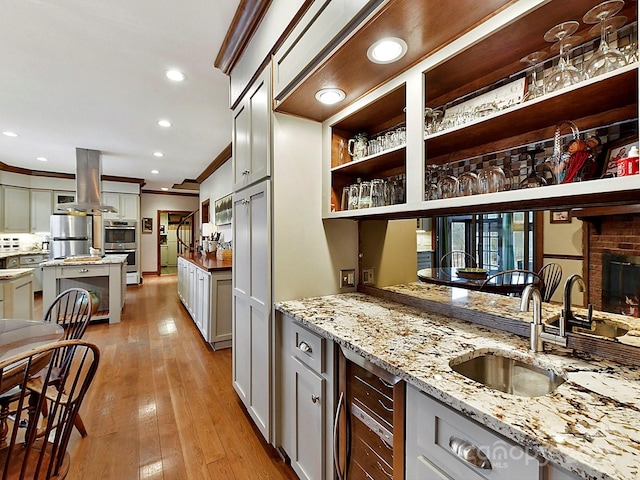 kitchen with sink, ornamental molding, island exhaust hood, stainless steel appliances, and light stone countertops