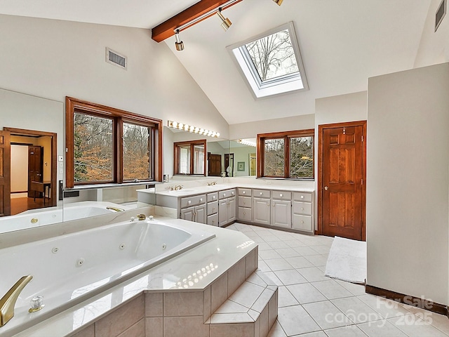 bathroom with vanity, vaulted ceiling with skylight, tile patterned flooring, and tiled tub