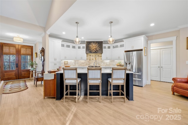 kitchen with pendant lighting, stainless steel fridge, white cabinetry, tasteful backsplash, and a center island with sink