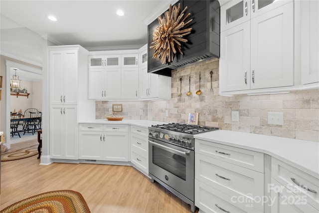 kitchen with high end stainless steel range oven, light wood-type flooring, white cabinetry, and wall chimney range hood