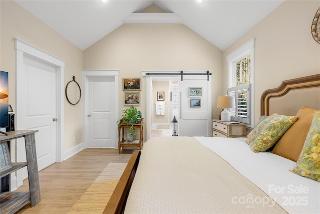 bedroom featuring light hardwood / wood-style floors, ensuite bathroom, lofted ceiling, and a barn door