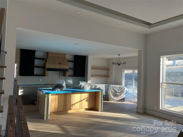 kitchen featuring light brown cabinetry, a chandelier, and custom exhaust hood