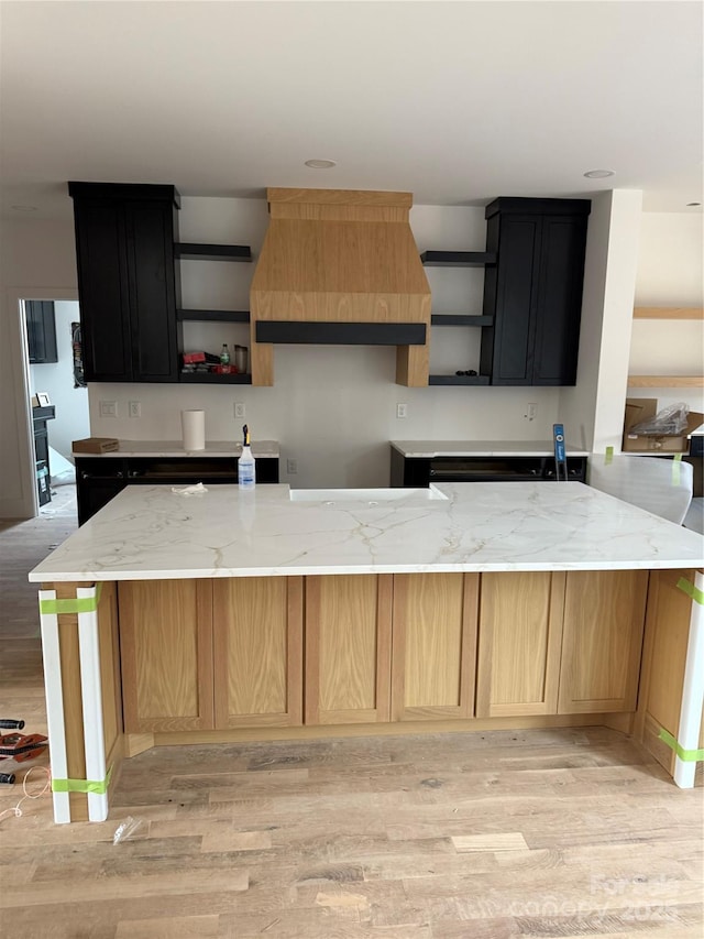 kitchen featuring premium range hood, light stone countertops, and light hardwood / wood-style floors