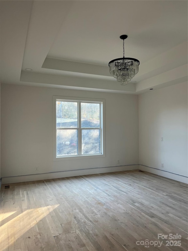 empty room featuring a tray ceiling, light hardwood / wood-style floors, and a chandelier