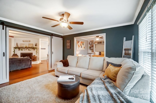 living room with wood-type flooring, ornamental molding, a barn door, and ceiling fan