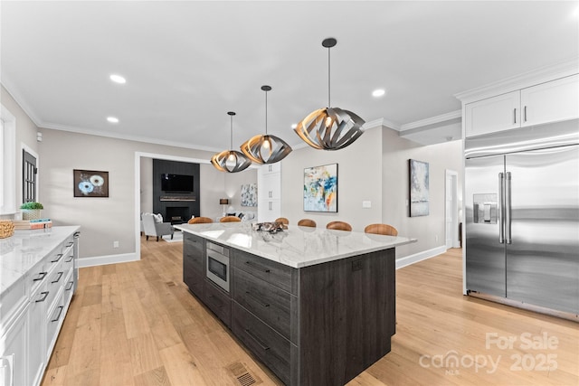 kitchen featuring built in appliances, white cabinetry, ornamental molding, and light stone countertops