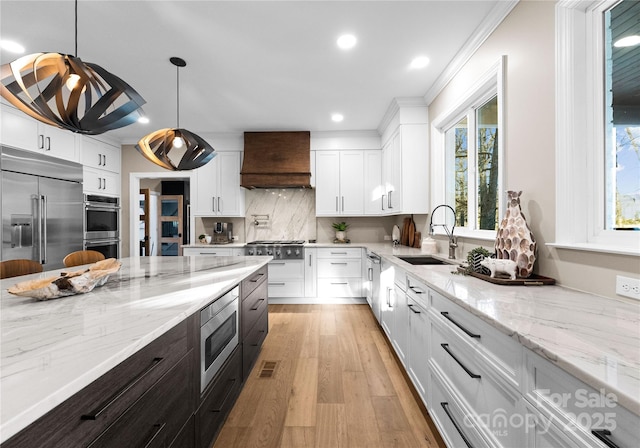 kitchen with sink, white cabinets, built in appliances, and custom range hood