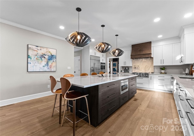 kitchen featuring built in appliances, a kitchen island, custom exhaust hood, and white cabinets