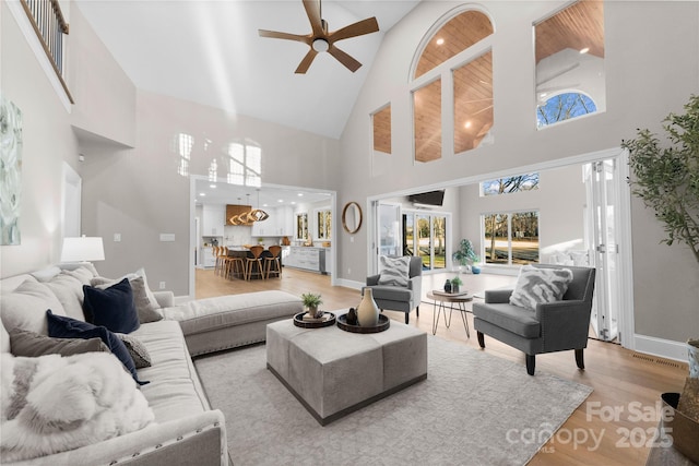 living room with ceiling fan, a high ceiling, wood ceiling, and light wood-type flooring