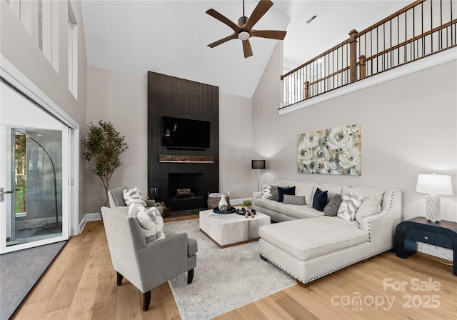 living room with ceiling fan, a wealth of natural light, hardwood / wood-style floors, high vaulted ceiling, and a large fireplace