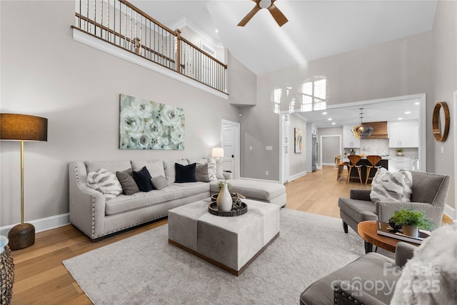 living room with ceiling fan, a high ceiling, and light wood-type flooring