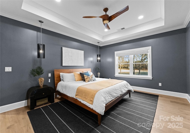 bedroom with ceiling fan, wood-type flooring, a tray ceiling, and crown molding