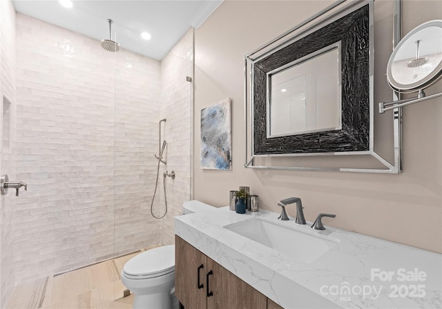 bathroom featuring toilet, tiled shower, ornamental molding, and vanity