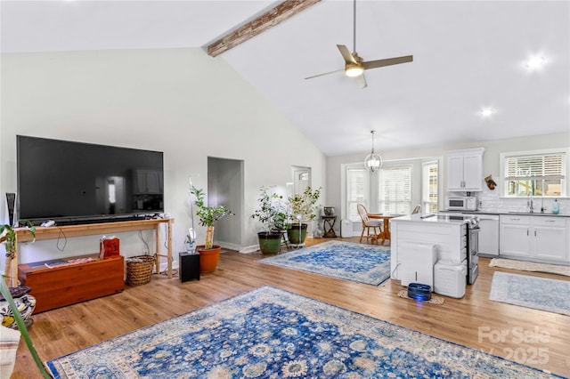 living room featuring beamed ceiling, a wealth of natural light, and light wood-type flooring