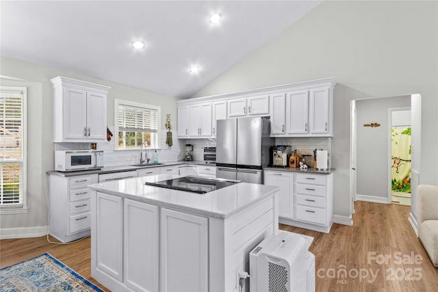 kitchen featuring stainless steel refrigerator, white cabinetry, sink, a center island, and black electric stovetop