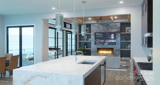 kitchen with pendant lighting, sink, a premium fireplace, light hardwood / wood-style floors, and an island with sink