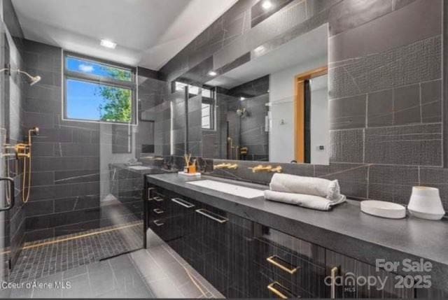 bathroom featuring a shower with door, vanity, tile patterned flooring, and tile walls