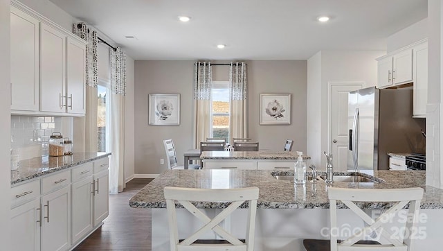 kitchen with sink, backsplash, stainless steel fridge, a kitchen breakfast bar, and a center island with sink