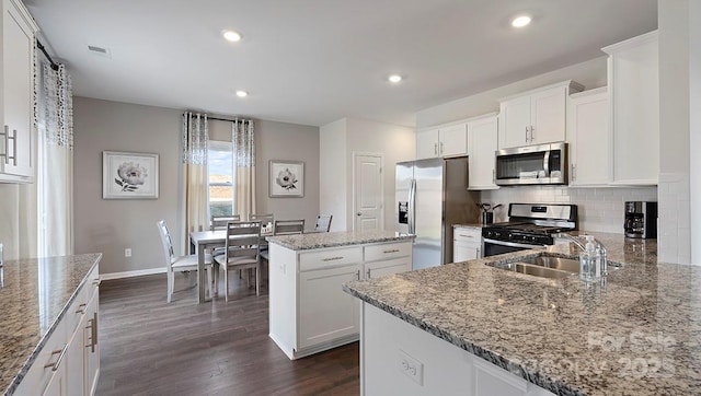 kitchen with light stone counters, white cabinetry, appliances with stainless steel finishes, and a kitchen island