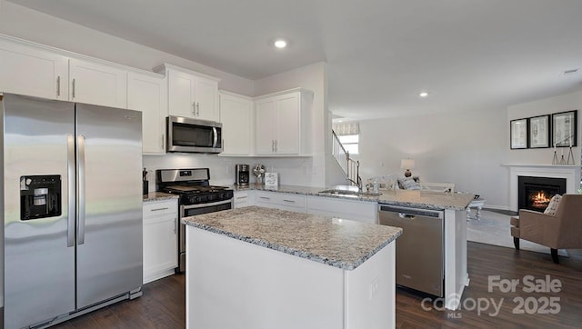 kitchen featuring a center island, appliances with stainless steel finishes, white cabinets, sink, and light stone counters