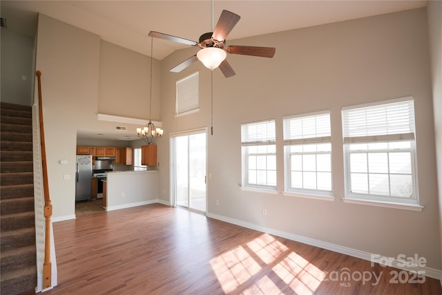 unfurnished living room with wood-type flooring, ceiling fan with notable chandelier, and a high ceiling