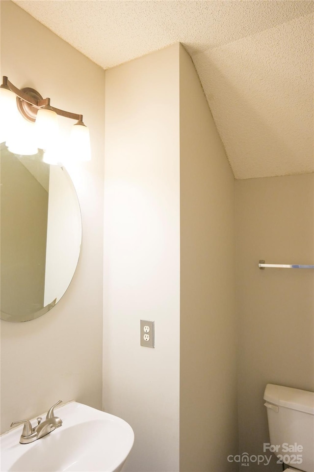 bathroom featuring lofted ceiling, sink, toilet, and a textured ceiling