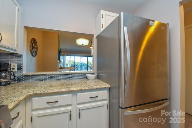 kitchen featuring white cabinetry, stainless steel refrigerator, decorative backsplash, and light stone counters