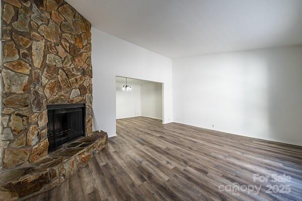 unfurnished living room featuring a notable chandelier, a stone fireplace, and wood-type flooring