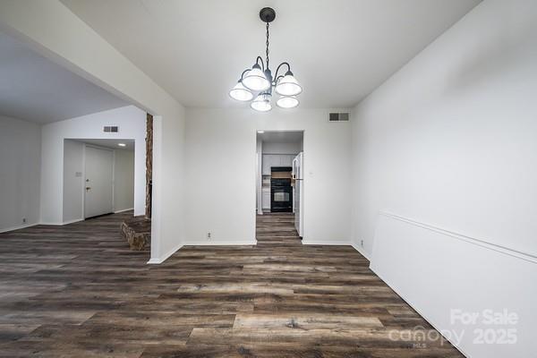 unfurnished dining area featuring dark wood-type flooring and an inviting chandelier