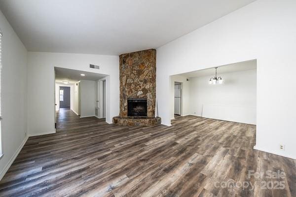 unfurnished living room featuring dark wood-type flooring, lofted ceiling, a stone fireplace, and an inviting chandelier