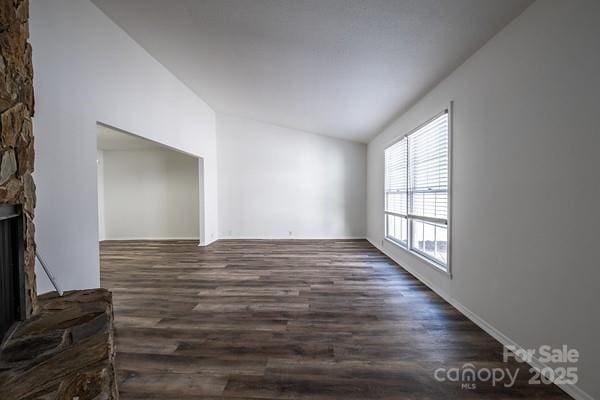 unfurnished living room featuring dark hardwood / wood-style flooring, a stone fireplace, and lofted ceiling