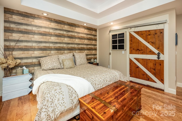 bedroom with a barn door, wood walls, and light hardwood / wood-style floors