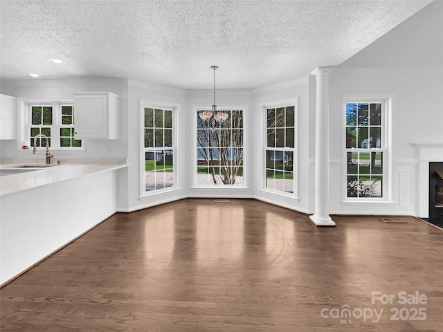 unfurnished dining area featuring ornate columns, a textured ceiling, sink, an inviting chandelier, and dark hardwood / wood-style floors