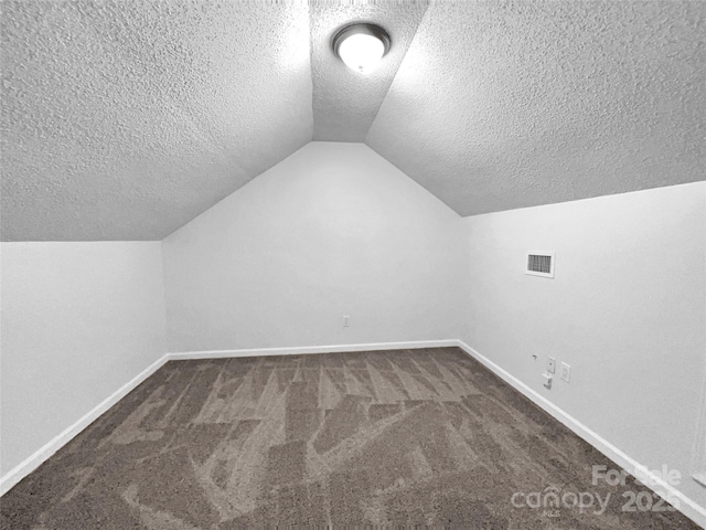 bonus room featuring vaulted ceiling, dark carpet, and a textured ceiling