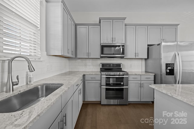 kitchen with stainless steel appliances, light stone countertops, sink, and gray cabinets