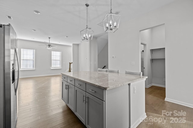 kitchen featuring gray cabinetry, a center island, stainless steel fridge with ice dispenser, hanging light fixtures, and light stone countertops