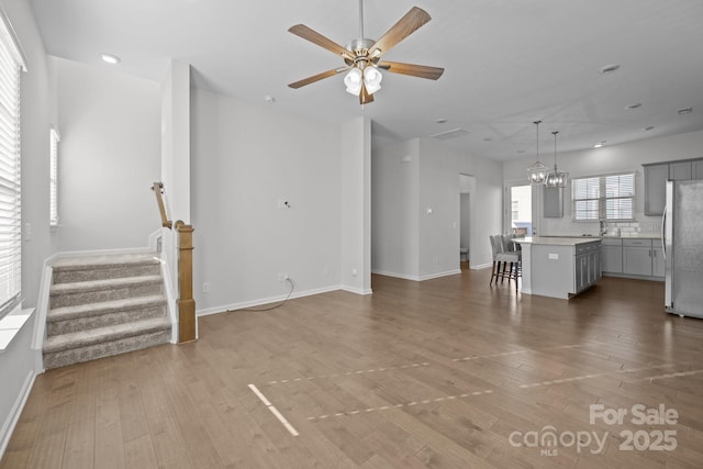 unfurnished living room featuring sink, hardwood / wood-style flooring, and ceiling fan with notable chandelier