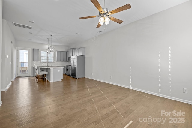 unfurnished living room with sink, ceiling fan with notable chandelier, and light hardwood / wood-style floors