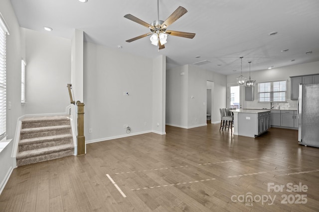 unfurnished living room featuring sink, ceiling fan with notable chandelier, and wood-type flooring