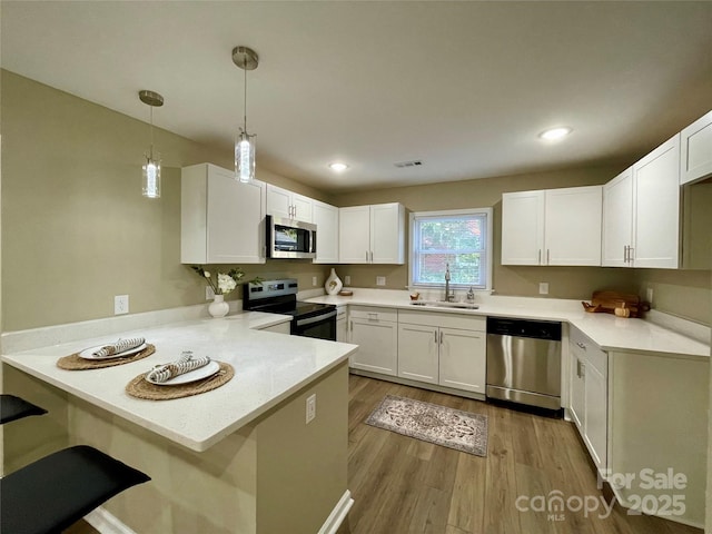 kitchen featuring appliances with stainless steel finishes, hanging light fixtures, white cabinets, sink, and kitchen peninsula