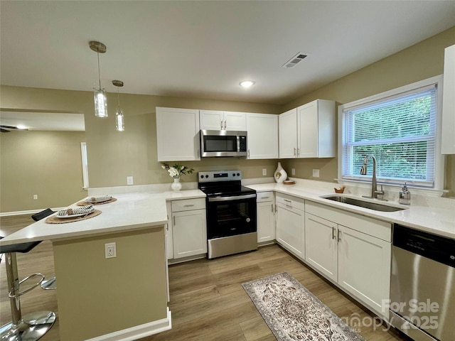 kitchen featuring kitchen peninsula, appliances with stainless steel finishes, sink, decorative light fixtures, and white cabinetry