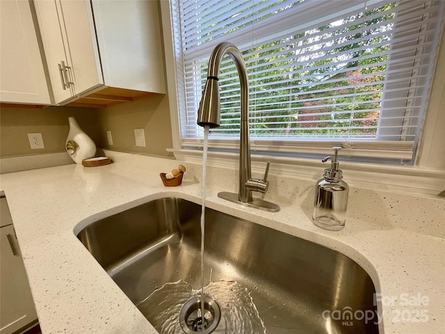 room details with light stone countertops, white cabinets, and sink