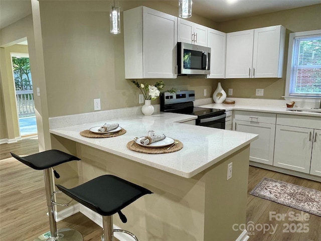 kitchen with kitchen peninsula, a kitchen breakfast bar, hanging light fixtures, white cabinets, and stainless steel appliances