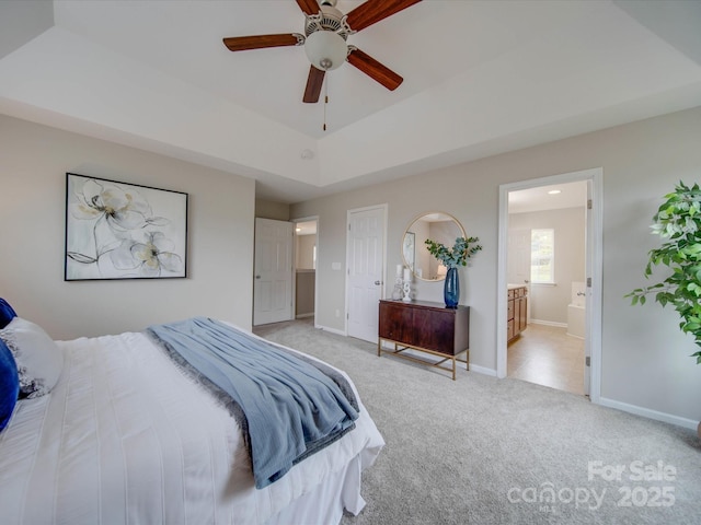 bedroom featuring ceiling fan, light colored carpet, a tray ceiling, and ensuite bathroom