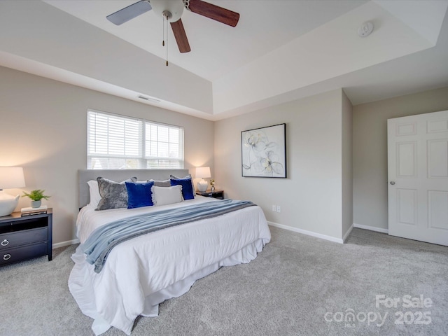 bedroom with ceiling fan, light colored carpet, and a tray ceiling