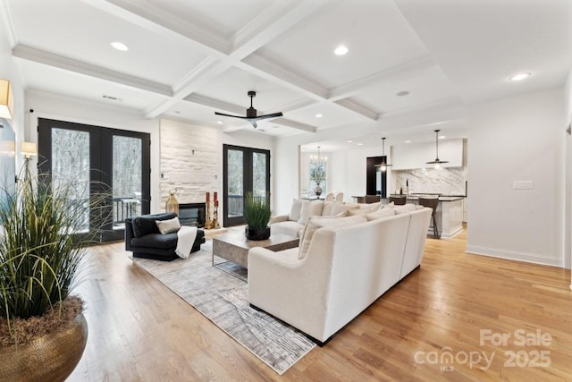 living room with light wood-style flooring, a fireplace, coffered ceiling, and french doors