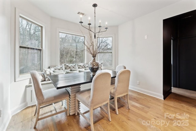 dining room with light wood-type flooring, a healthy amount of sunlight, baseboards, and a notable chandelier