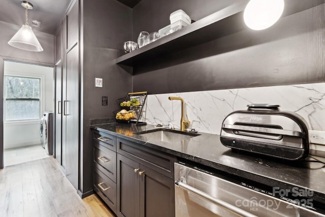 kitchen with tasteful backsplash, washer / clothes dryer, stainless steel dishwasher, a sink, and dark stone counters