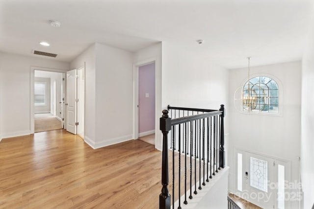 hall featuring light wood finished floors, baseboards, visible vents, an upstairs landing, and a notable chandelier