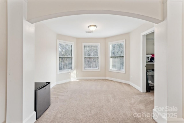 spare room with arched walkways, a healthy amount of sunlight, and light carpet